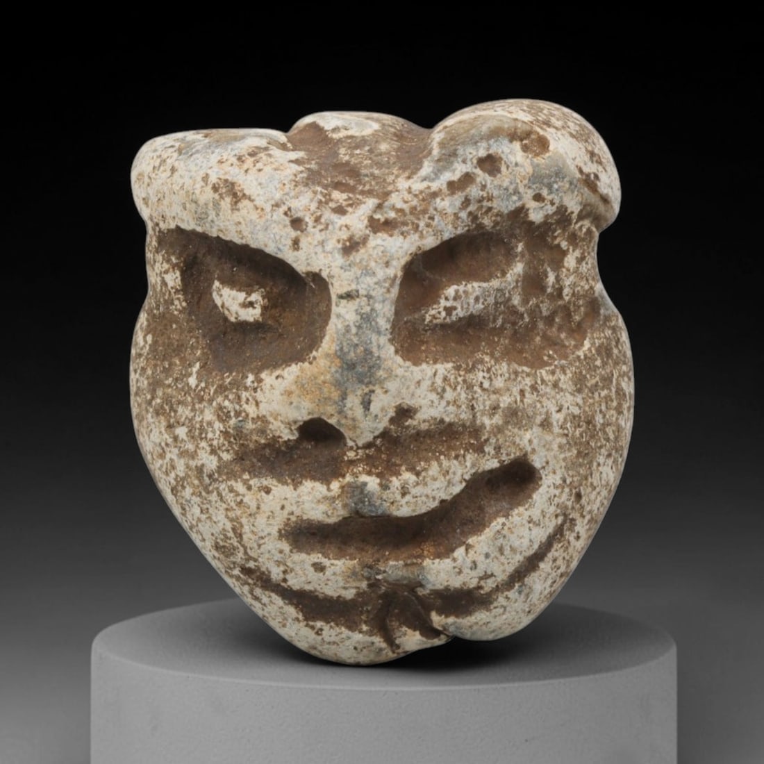 Ancient Stone Maskette - Medieval Grotesque Face Figurine, 39BH: A carved stone maskette of rounded form, fashioned from a single piece of weathered limestone with natural white and brown mineral encrustation. The front is carved in deep relief to depict a stylized