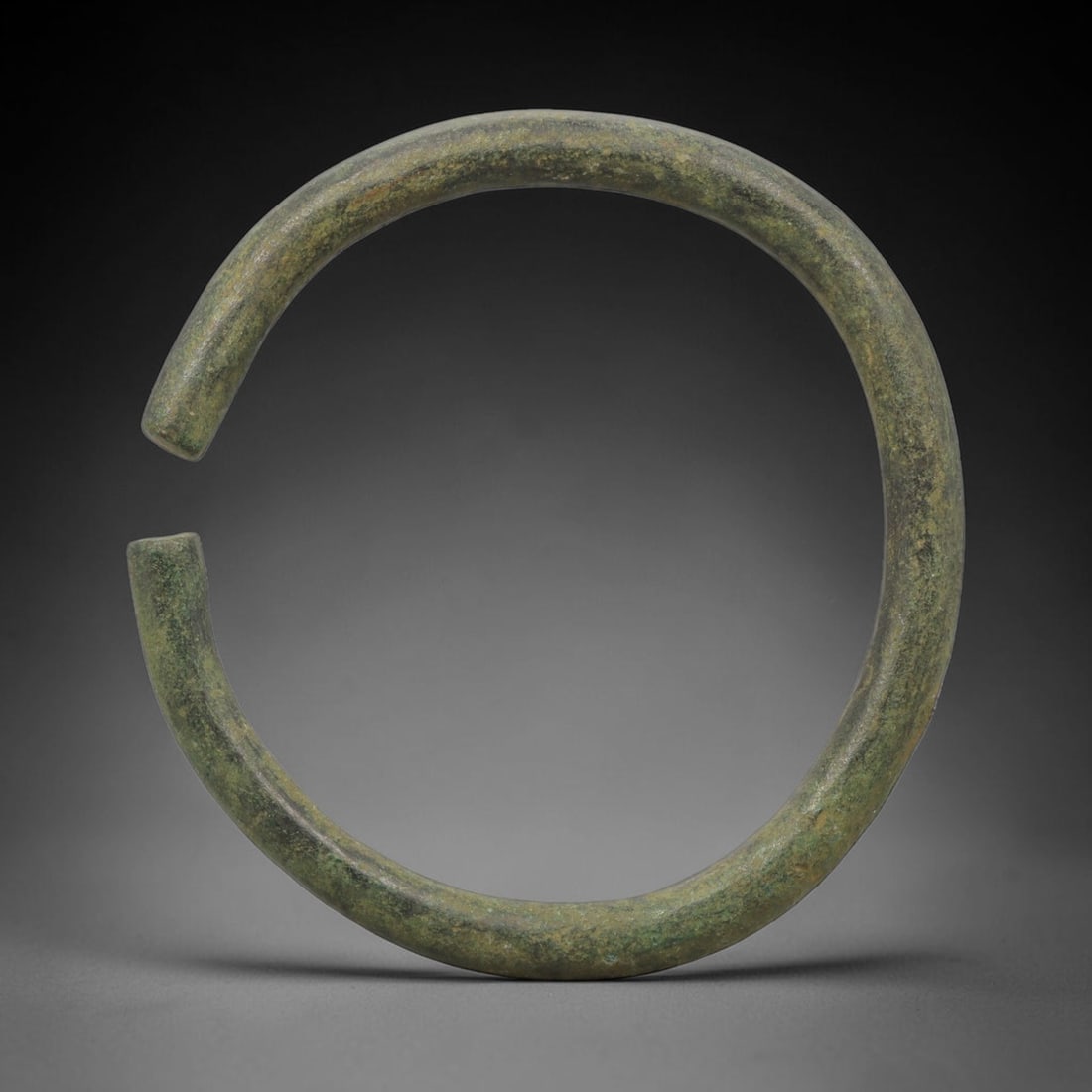 Ancient Bronze Bracelet - Roman Plain Cuff Armlet, 18BH: A cast bronze open-cuff bracelet of circular form, constructed from a thick, solid bronze band with a simple open terminal design for wear. The piece is unadorned, with a smooth, rounded profile chara
