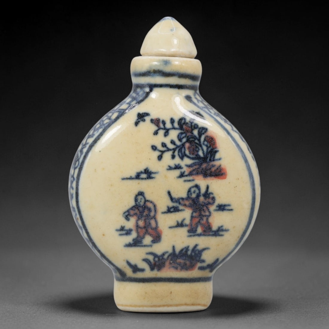 A Chinese Porcelain Snuff Bottle, 20th Century, 10YD: Crafted from porcelain with a pale cream glaze and decorated in underglaze blue with copper red accents, the snuff bottle features a flattened, rounded body, a short cylindrical neck, and a conical st