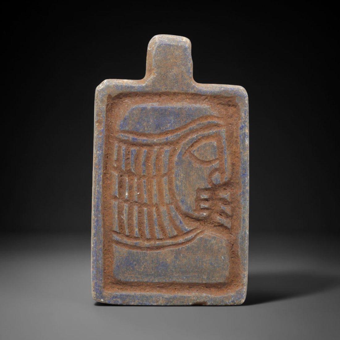 Near Eastern Lapis Lazuli Amulet - Tribal Art Face Relief Pendant, 50ZY: Carved from lapis lazuli, this rectangular amulet features a deeply incised relief depiction of a stylized facial profile, rendered in a geometric tribal idiom. The face is defined by linear detailing