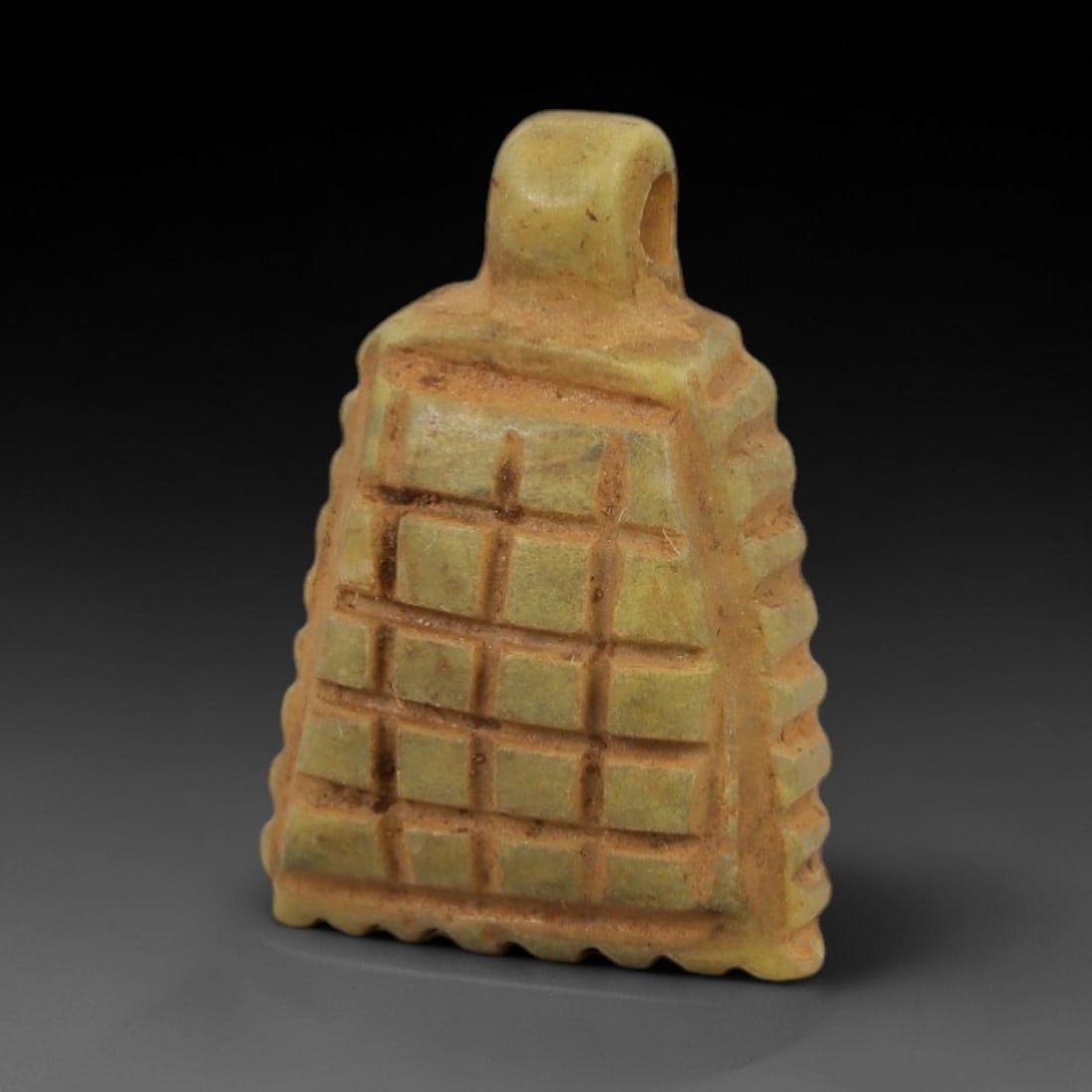 Ancient Egyptian Stone Amulet - Carved Ritual Pendant, 57AE: Carved from beige stone, this amulet features a geometric grid pattern with a suspension loop at the top, consistent with ancient Egyptian ritual pendants of the Late Period. The form is designed for