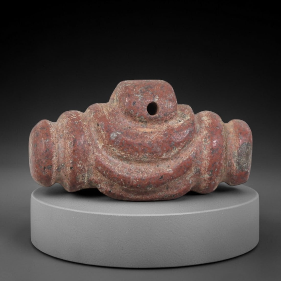 Ancient Stone Amulet - Egyptian Ritual Relic, 79AP: This artifact is carved from red stone with a textured, weathered surface showing natural patina and subtle mineral inclusions indicative of age. The form features a symmetrical, ribbed structure with