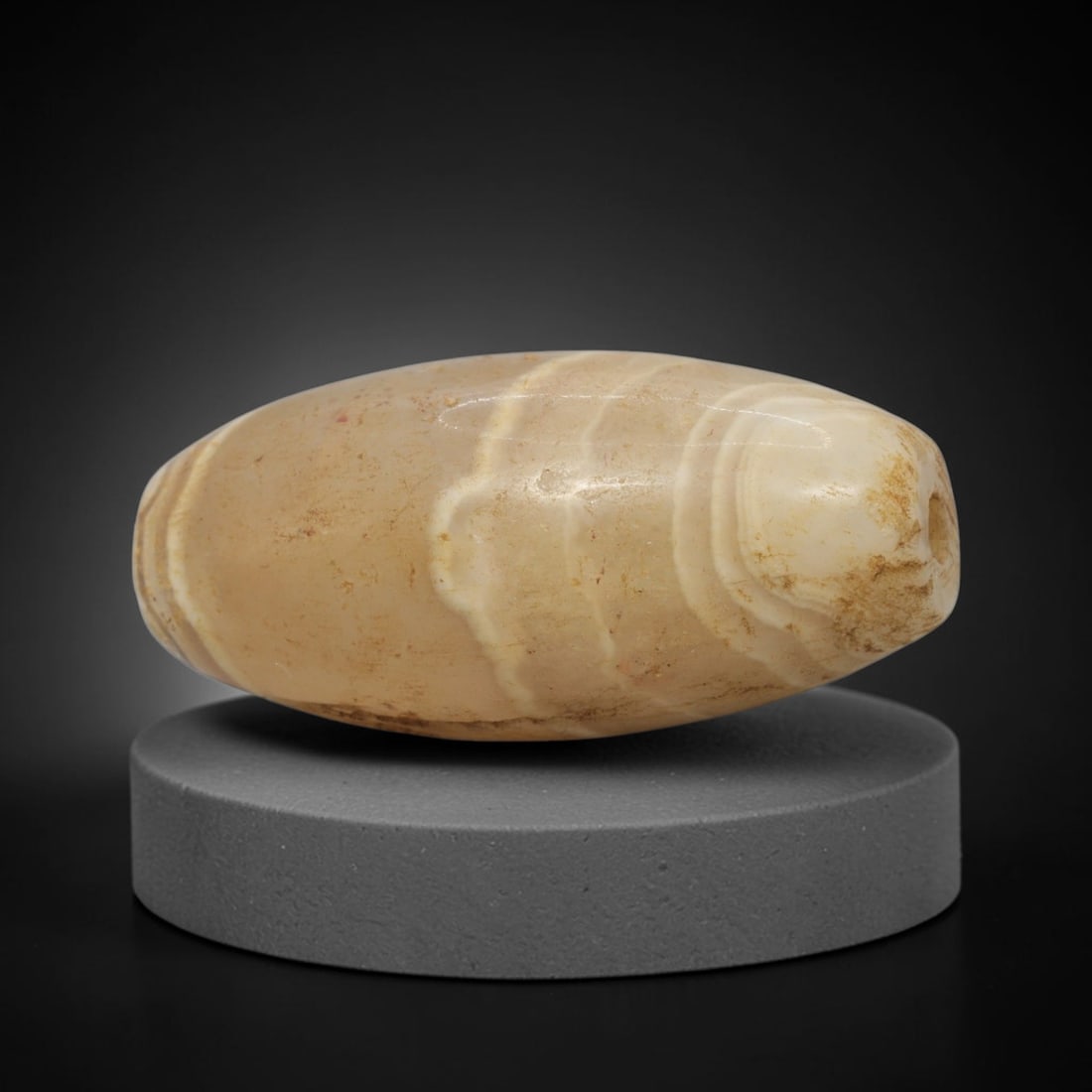 Ancient Agate Bead - Indus Valley Banded Carving, 69WJ: This artifact is crafted from banded agate, exhibiting subtle, flowing concentric banding in warm cream and pale amber tones across its polished surface. The bead is shaped in an elongated, bicone bar