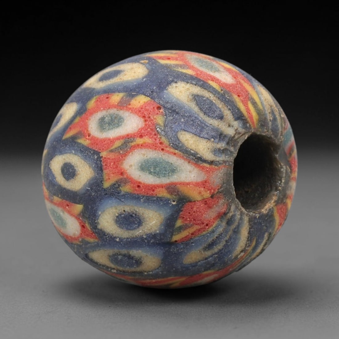 Ancient Mosaic Glass Bead - Roman Eye Pattern Amulet, 57WD: This spherical bead is crafted from core-formed mosaic glass, featuring a deep indigo blue base decorated with repeating concentric eye motifs. Each motif consists of a central glass circle in shades