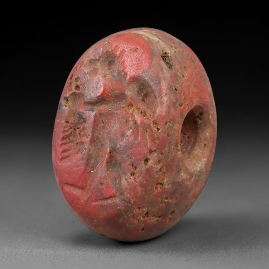 Ancient Jasper Stamp Seal - Near Eastern Anthropomorphic Figure, 99AM: Carved from porous red jasper, this hemispherical stamp seal depicts a stylized anthropomorphic figure with incised linear details defining its torso, limbs, and facial elements. The iconography align