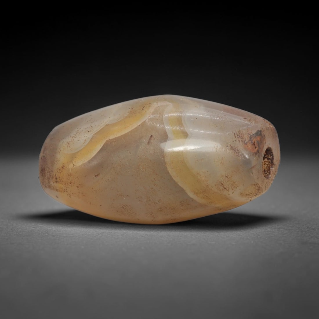 Ancient Agate Bead - Indus Valley Banded Carving, 79WJ: This artifact is crafted from banded agate, featuring soft, flowing concentric banding in warm amber and creamy white tones across its polished, rounded surface. The bead is shaped in a smooth, barrel