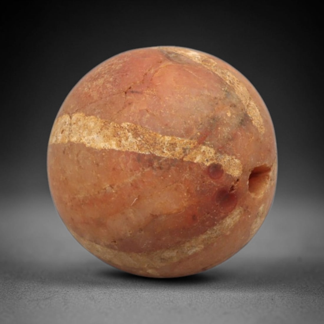 Ancient Carnelian Etched Bead - Gandhara Spherical Bead, 20XY: The bead is crafted from carnelian, a semi-precious chalcedony, with a spherical form and laterally drilled suspension hole. Its surface features an etched white pattern of horizontal banded motifs, c
