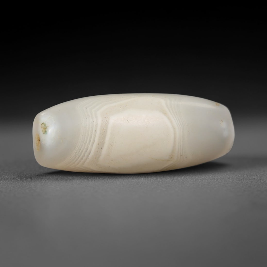 Ancient Agate Bead - Indus Valley Amulet, 53BC: This artifact is crafted from creamy white banded agate, exhibiting fine concentric layered striations across its smooth barrel-shaped form, shaped through skilled ancient lapidary work. The bead feat