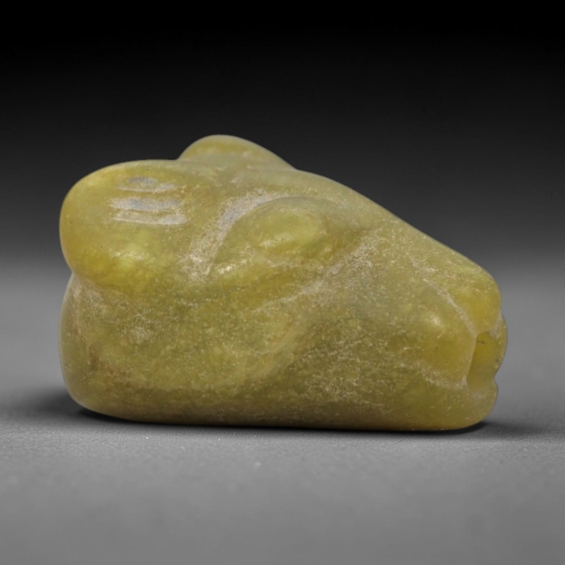 Ancient Serpentine Zoomorphic - Near Eastern Amulet Figurine, 81ZW: This amulet is carved from pale yellow-green serpentine, shaped into a stylized zoomorphic head, likely representing a canine or feline creature linked to protective symbolism in ancient Near Eastern