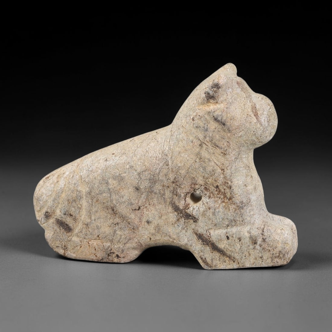 Ancient Schist Recumbent Feline Amulet - Near Eastern Carved Figurine, 55BA: Carved from schist, this amulet takes the form of a stylized recumbent feline (likely a lion or protective beast), rendered in three dimensions with simplified, bold carving. A drilled suspension hole