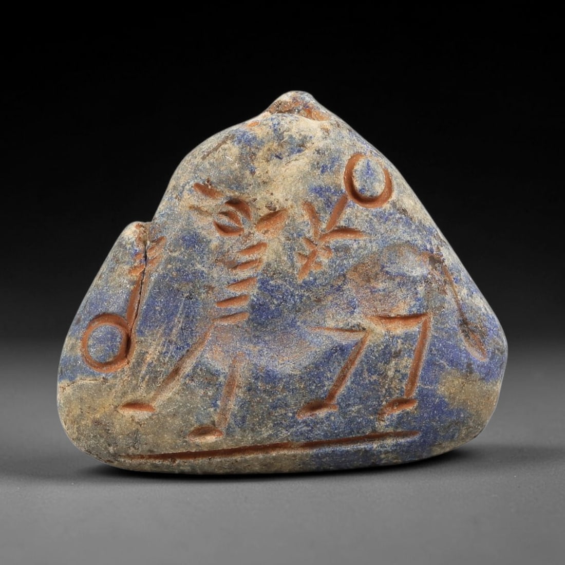 Ancient Lapis Lazuli Amulet - Near Eastern Animal Figurine, 35BA: Carved from lapis lazuli, the amulet takes a triangular, mountain-shaped form with a small suspension loop at the top, designed for wear as a protective talisman. The front face is incised with a styl