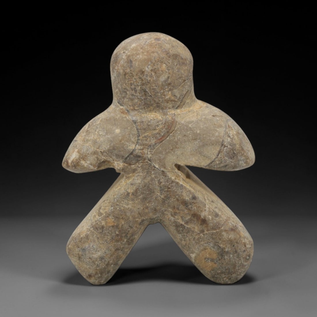 Ancient Stone Abstract Figurine - Near Eastern Idol, 84XQ: Carved from a mottled grey-brown stone, this artifact depicts a highly stylized abstract humanoid figurine with a rounded head, broad outstretched arms, and thick splayed legs forming a stable base. T