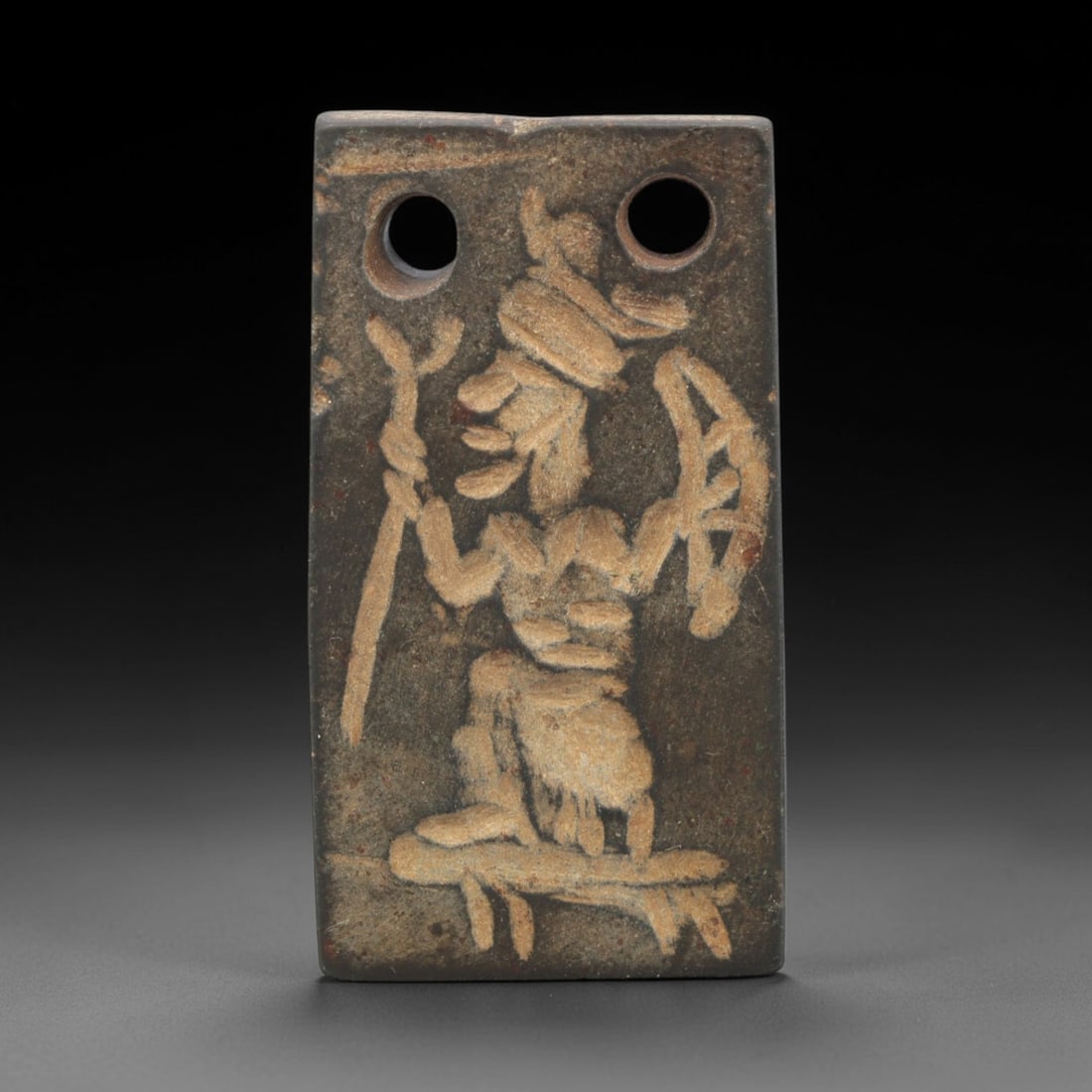 Ancient Steatite Plaque - Near Eastern Deity Figurine, 14AK: Carved from steatite, this rectangular plaque features a low-relief scene depicting a kneeling male figure, likely a deity or ritual attendant, holding a staff and bow-like object, with a headdress an