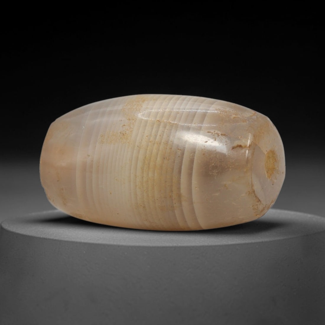 Ancient Agate Bead - Indus Valley Banded Carving, 67WJ: This artifact is crafted from banded agate, exhibiting fine, parallel concentric banding in warm creamy beige and pale translucent tones across its polished surface. The bead is shaped in a smooth, ba