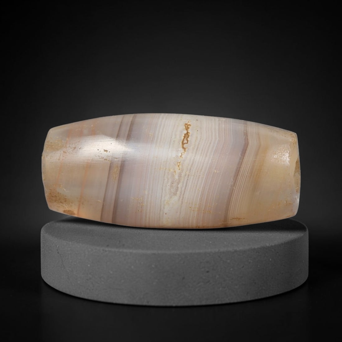 Ancient Banded Agate Bead - Near Eastern Artifact, 66BD: This artifact is crafted from natural banded agate, shaped into an elongated barrel form with fine, parallel concentric banding in warm taupe, cream, and amber hues. The bead features a central perfor