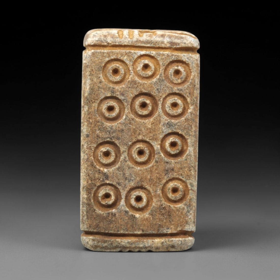 Ancient Steatite Amulet - Near Eastern Concentric Circles Bead, 55XV: This artifact is carved from steatite, exhibiting uniform, precise craftsmanship across its rectangular form. Its primary decorative motif consists of concentric circle carvings arranged in a grid pat