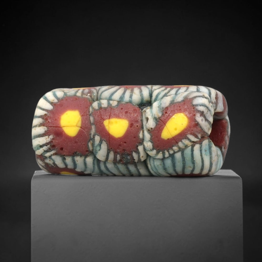 Ancient Roman Mosaic Glass Bead - Floral Eye Pattern Amulet, 76WD: This rectangular mosaic glass bead is crafted from core-formed glass, featuring repeating floral eye motifs across its surface. Each motif consists of a central yellow glass inlay set within a deep re