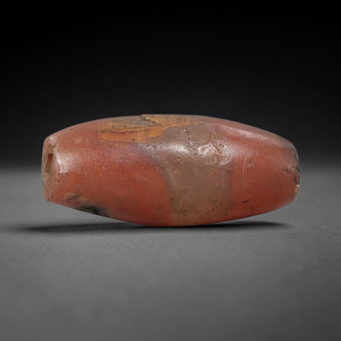 Ancient Carnelian Agate Bead - Near Eastern Artifact, 22BC: This artifact is crafted from natural carnelian (red agate), shaped into an elongated tapered barrel form with a rich warm red base and subtle natural banding. The bead features a central perforation