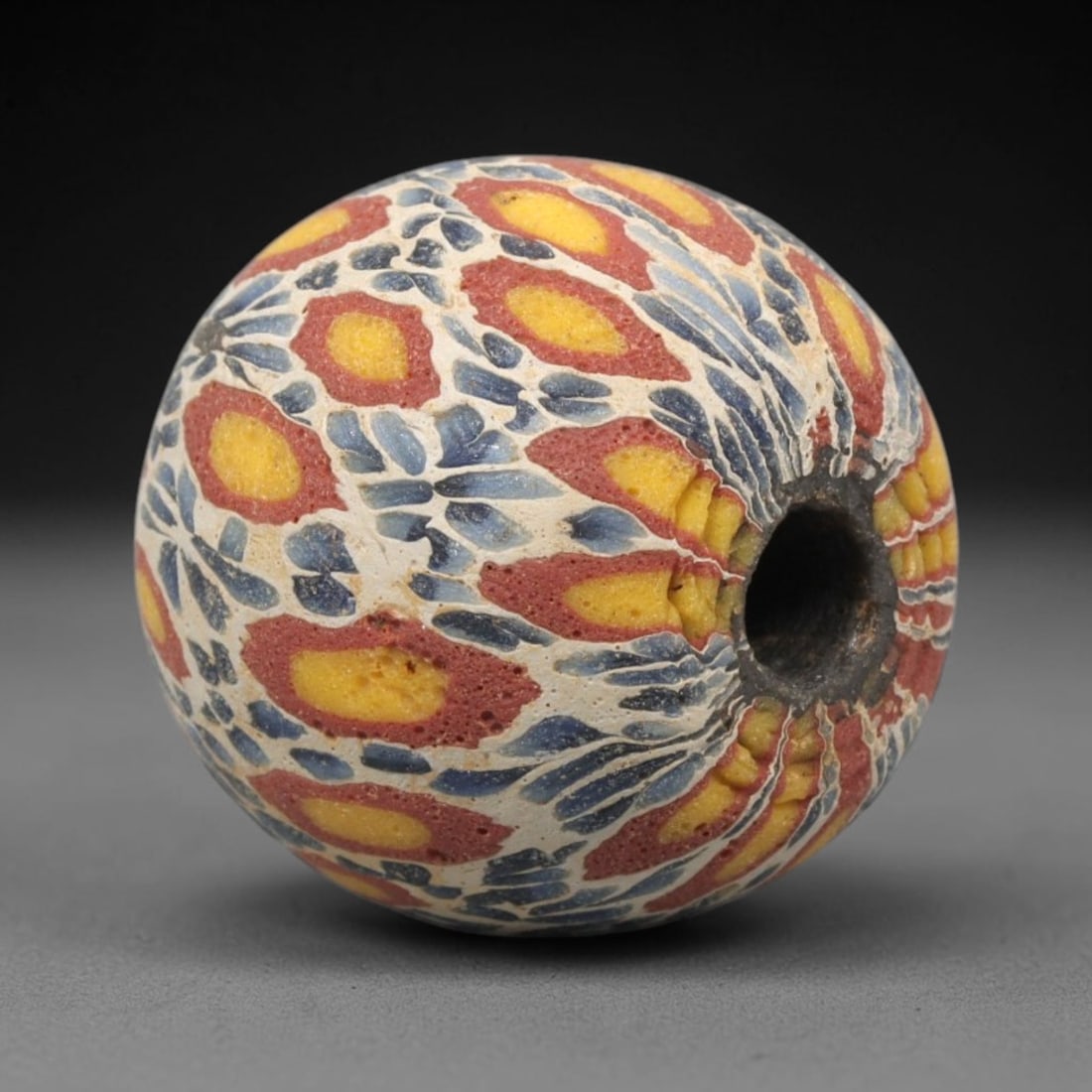 Ancient Mosaic Glass Bead - Roman Floral Pattern Amulet, 56WD: This spherical bead is crafted from core-formed mosaic glass, featuring a creamy white base decorated with intricate floral and foliate motifs. Each motif consists of a central yellow glass inlay outl