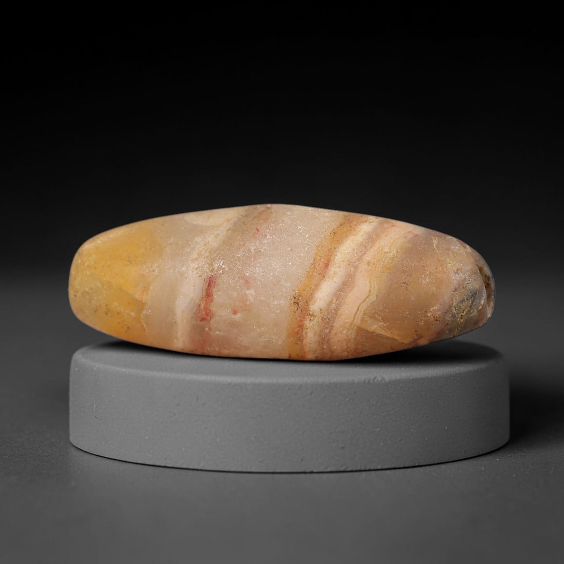 Ancient Banded Agate Bead - Indus Valley Artifact, 32BD: This artifact is crafted from natural banded agate, shaped into an elongated, tapered barrel form with striking concentric banding in warm amber, cream, and soft red hues. The bead features a central