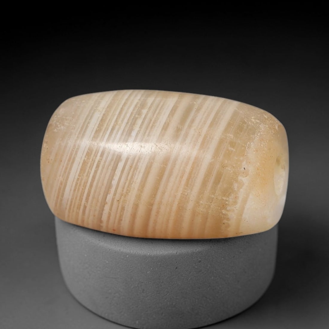 Ancient Agate Bead - Silk Road Artifact, 34BD: This artifact is crafted from banded agate, shaped into a short, rounded barrel form with delicate, evenly spaced concentric banding in pale cream and soft amber tones. The bead features a central per