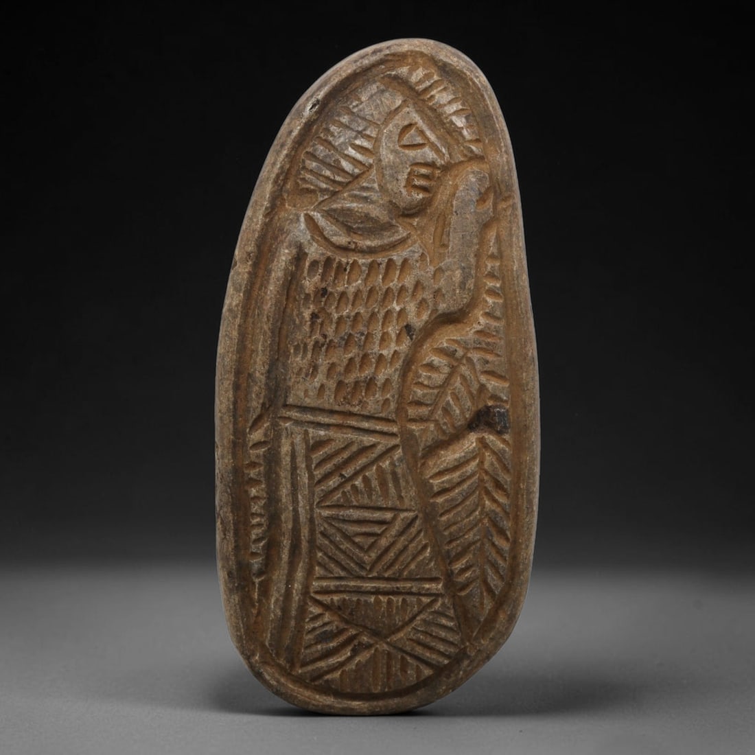 Ancient Stone Plaque Relief - Near Eastern Human Figural Plaque, 10ZY: Carved from a single piece of stone, this oval relief plaque depicts a stylized standing human figure in profile, rendered in the linear, incised artistic tradition of the ancient Near East. The figur