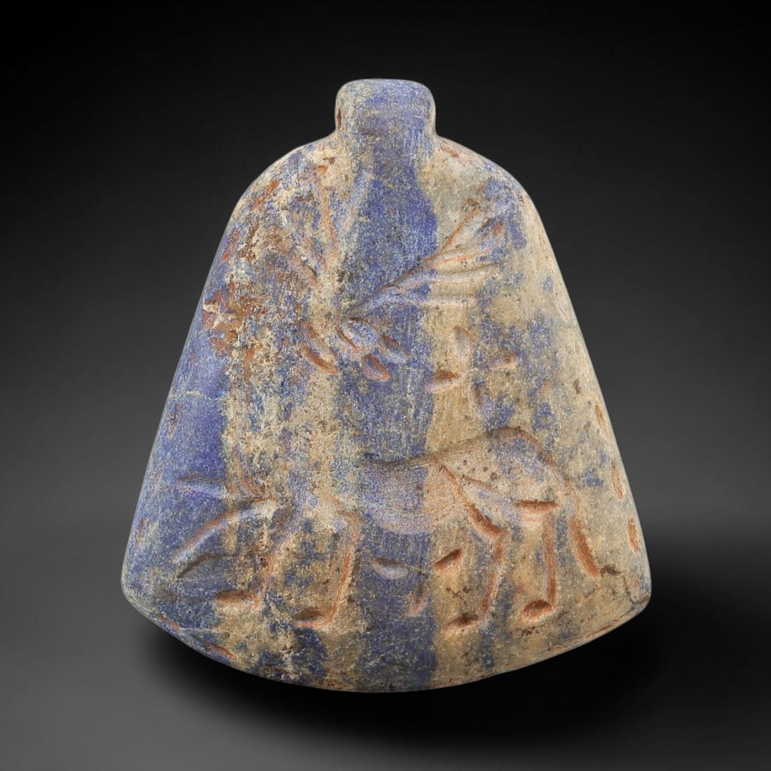 Ancient Lapis Lazuli Amulet - Near Eastern Animal Figurine, 54BA: Carved from lapis lazuli, the amulet takes a bell-shaped form with a suspension loop at the top, designed for wear as a protective talisman. The front face is incised with a stylized quadruped animal