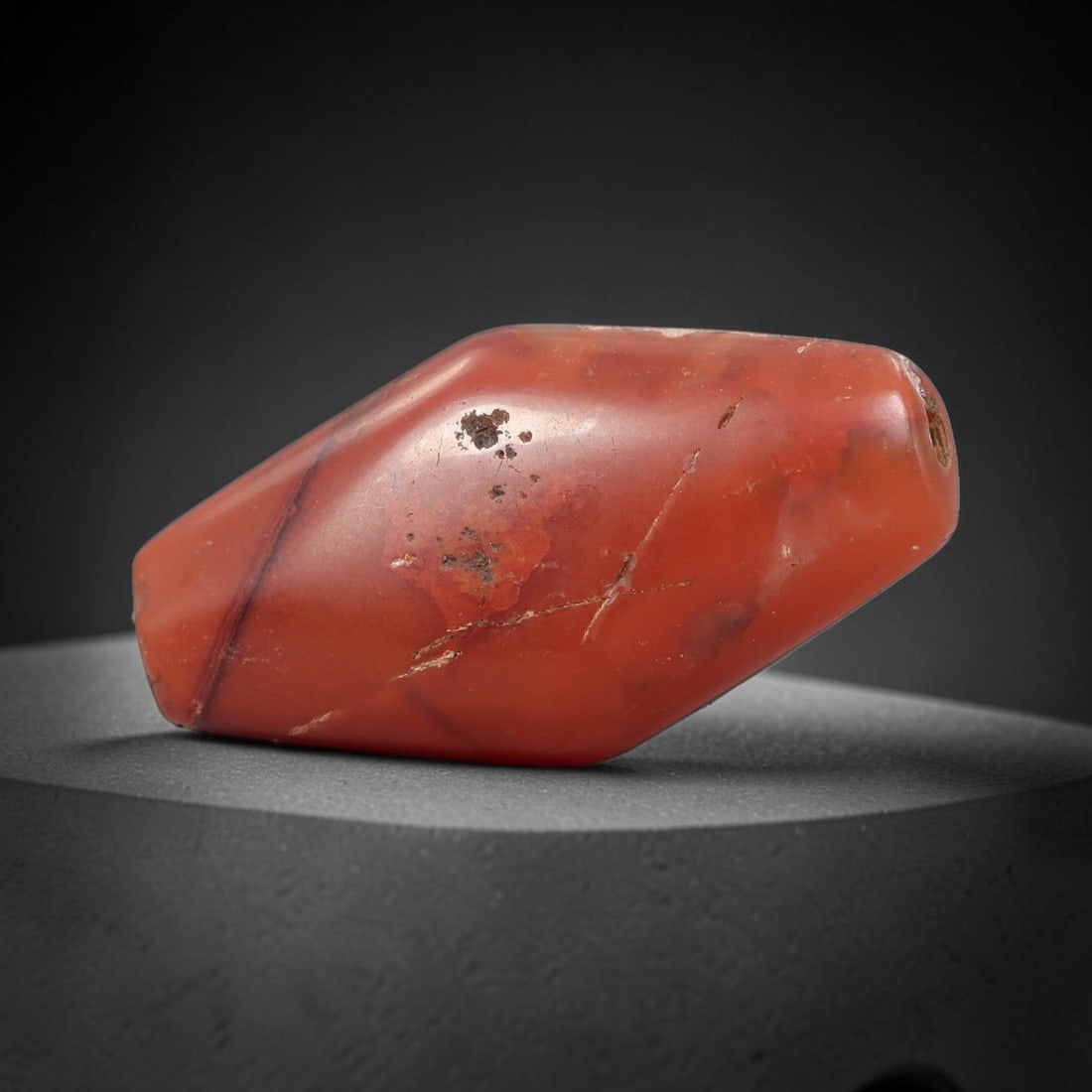 Ancient Carnelian Bead - Silk Road Bicone Amulet, 23BC: Carved from solid carnelian, the bead features a faceted bicone form with a smooth, polished surface that showcases the stone's deep, warm reddish-orange hue and natural internal veining. A longitudin