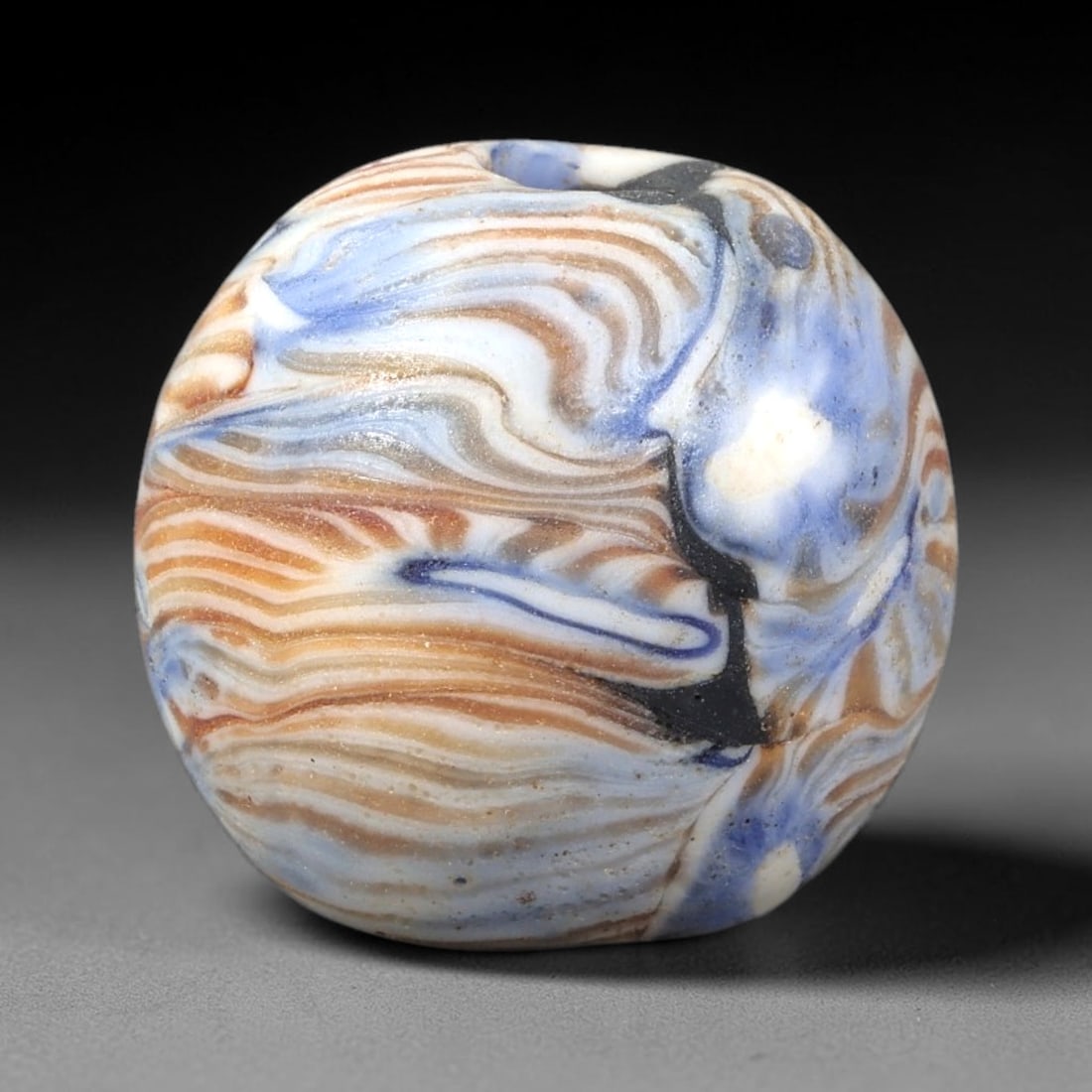 Ancient Glass Bead - Islamic Marbled Spherical Pendant, 17BG: A spherical ancient glass bead crafted with a marbled or agate-like glass technique, featuring swirling, layered patterns of opaque white, soft blue, and amber-brown glass, interwoven with thin black