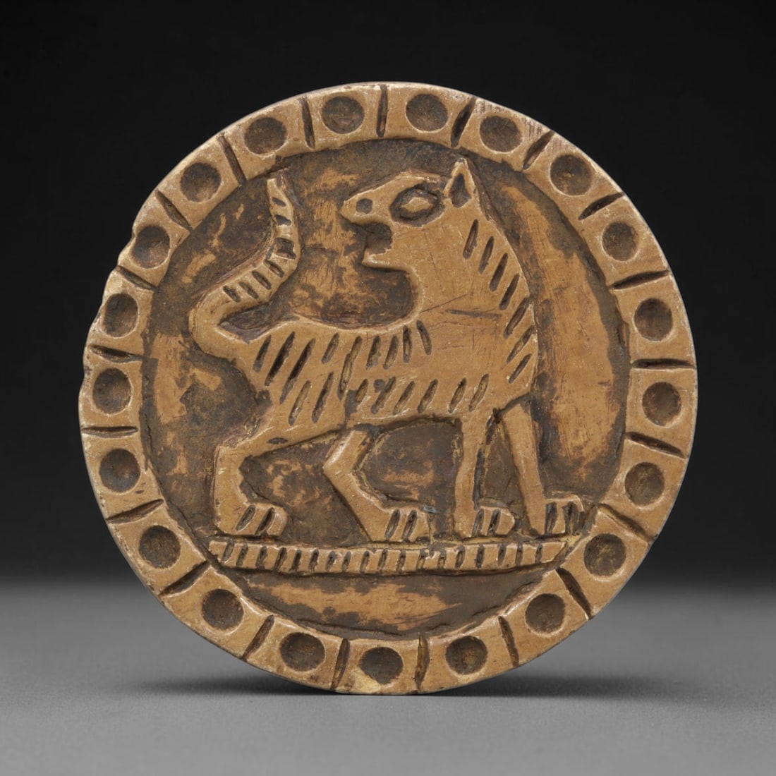 Ancient Steatite Plaque - Near Eastern Lion Relief, 24ZY: Carved from steatite, this circular plaque features a relief depiction of a stylized lion, rendered in the schematic artistic tradition of the Ancient Near East. The feline figure is shown standing in