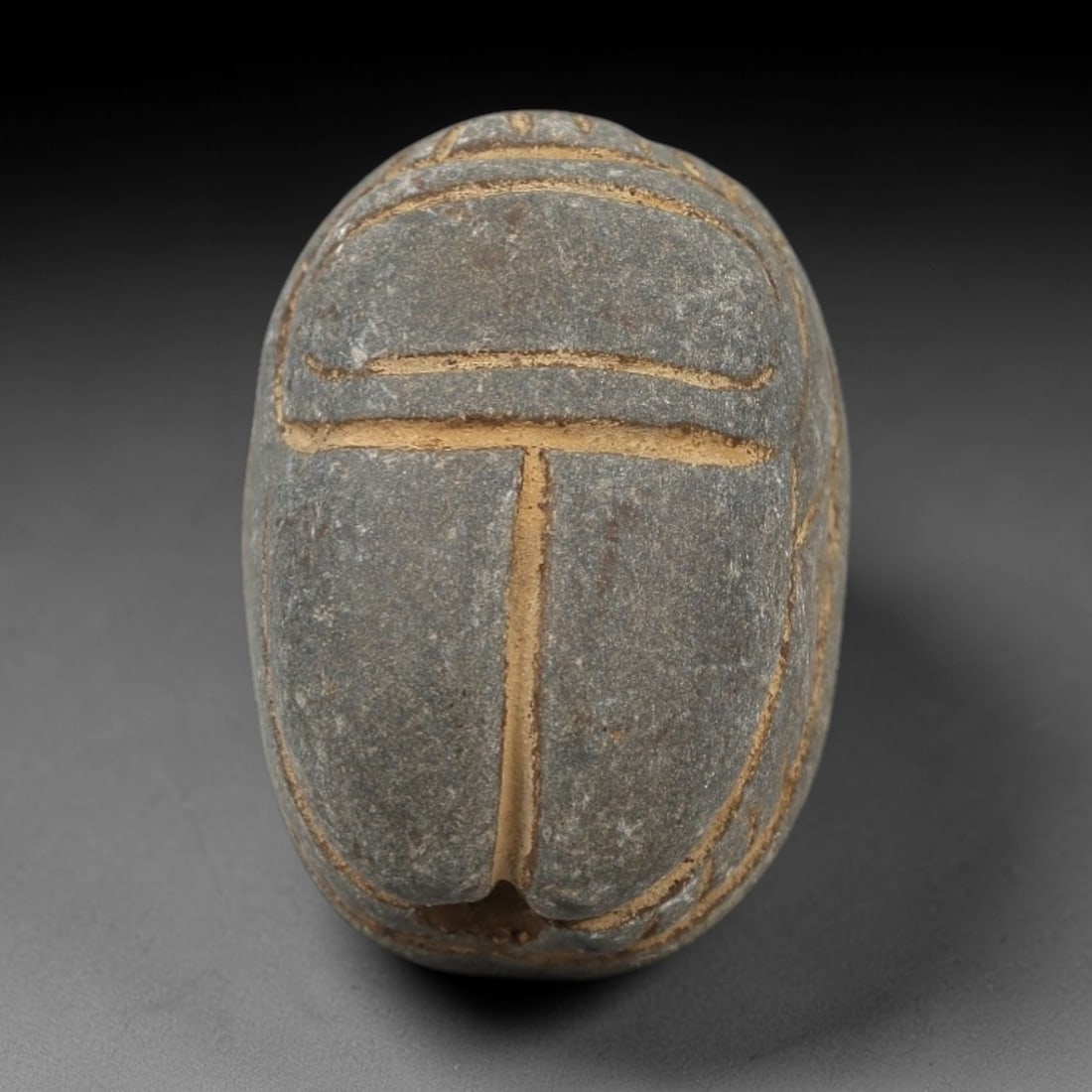 Ancient Egyptian Grey Stone Scarab - Amulet Figurine, 37AM: This artifact is a carved grey stone scarab amulet, crafted from a dense, dark grey stone with a matte surface and earthy patina filling the incised linear details. The dorsal side features bold, simp