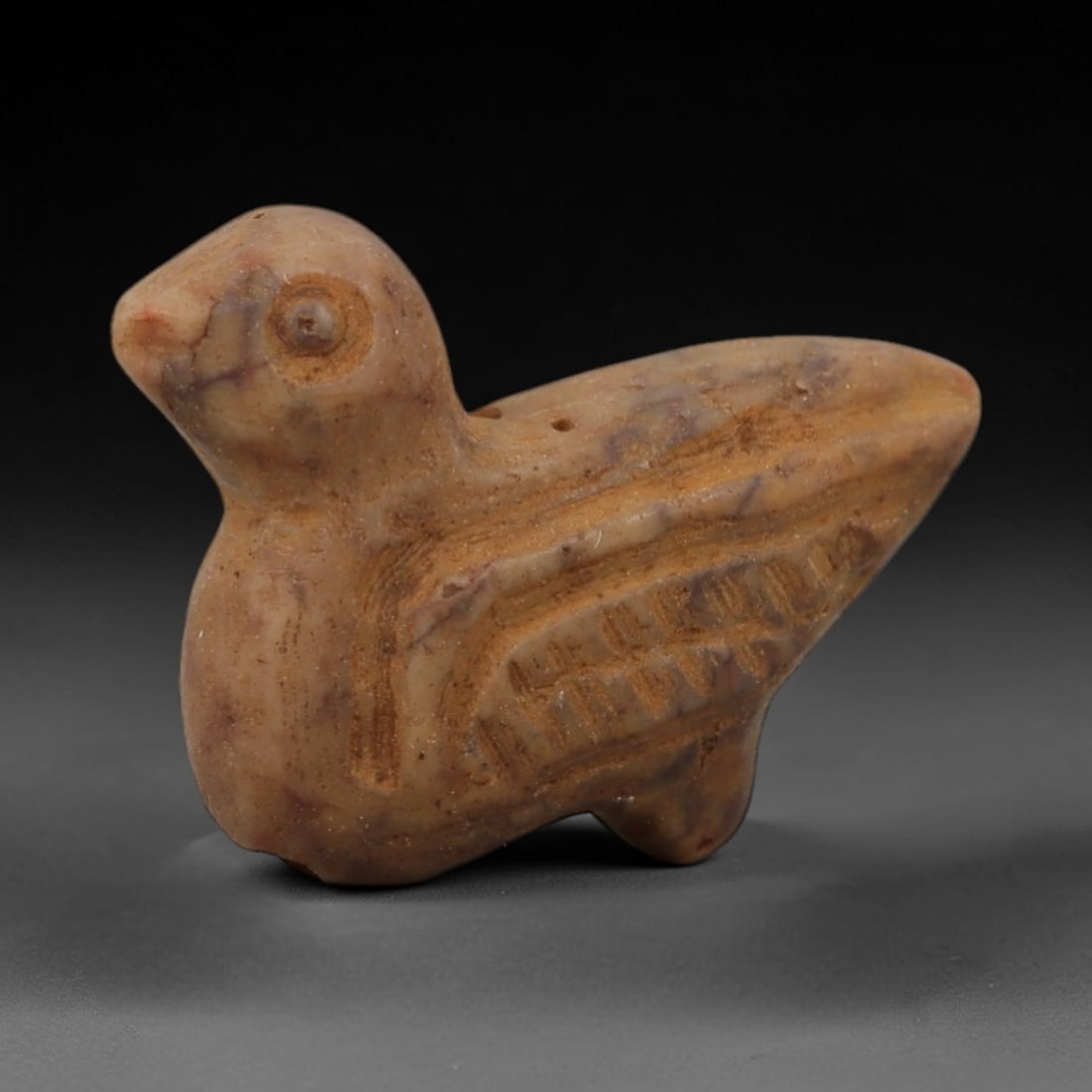 Ancient Mottled Stone Bird Amulet - Near Eastern Figurine, 91AD: Carved from mottled tan stone with subtle purple veining, this amulet depicts a stylized bird in a compact, upright form. The creature is rendered with a rounded head, incised eye detail, and detailed