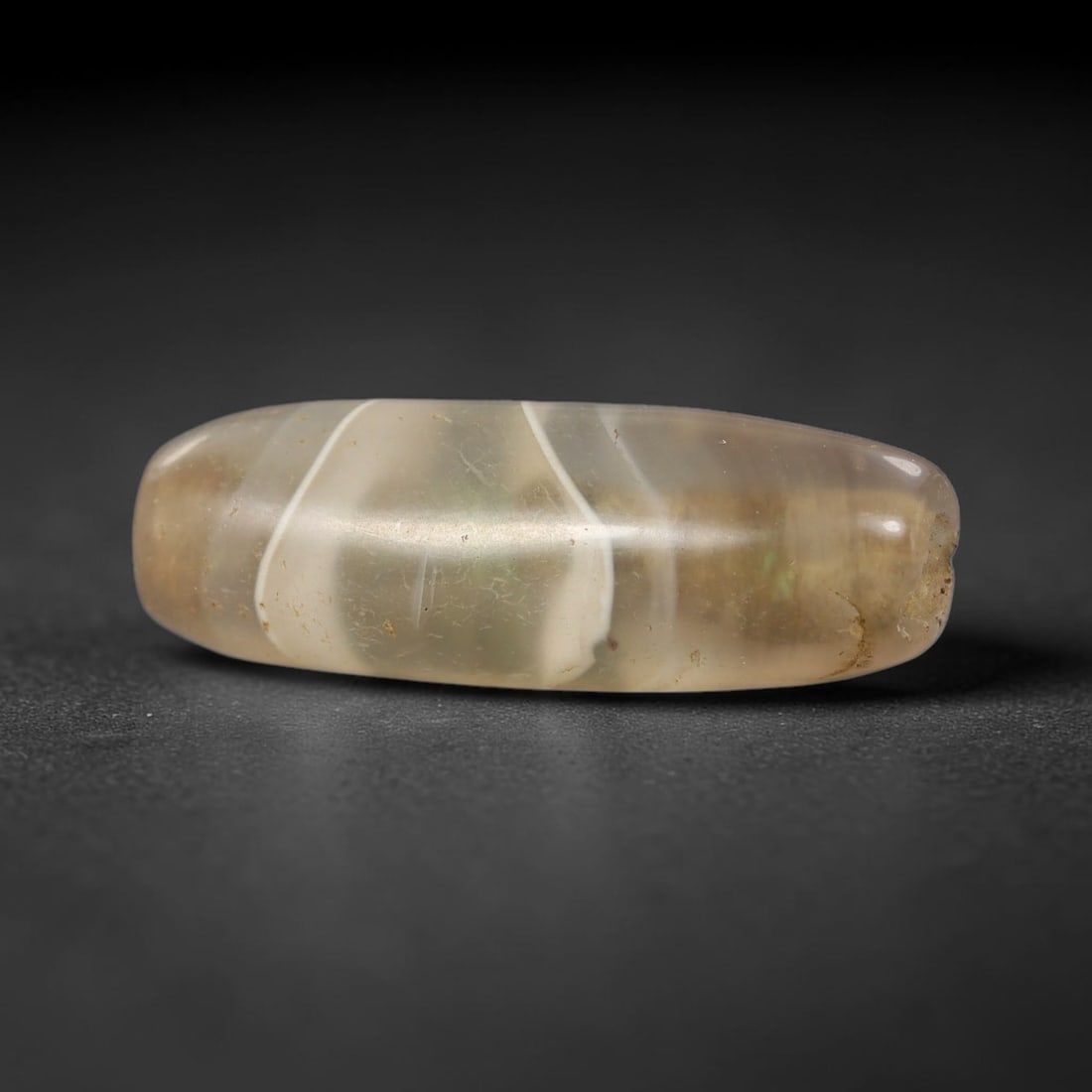Ancient Banded Agate Bead - Near Eastern Artifact, 100BD: This artifact is crafted from translucent banded agate, shaped into an elongated barrel form with striking white concentric banding against a pale smoky-grey base. The bead features a central perforat