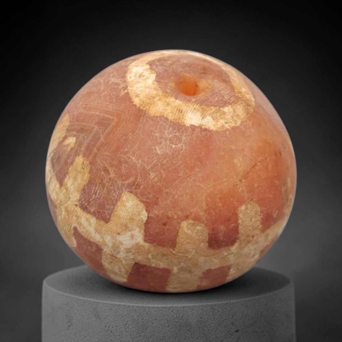 Ancient Carnelian Etched Bead - Gandhara Spherical Bead, 16XY: The bead is carved from carnelian, a semi-precious chalcedony, with a spherical form and a laterally drilled suspension hole. Its surface features an etched white geometric pattern of cross motifs and