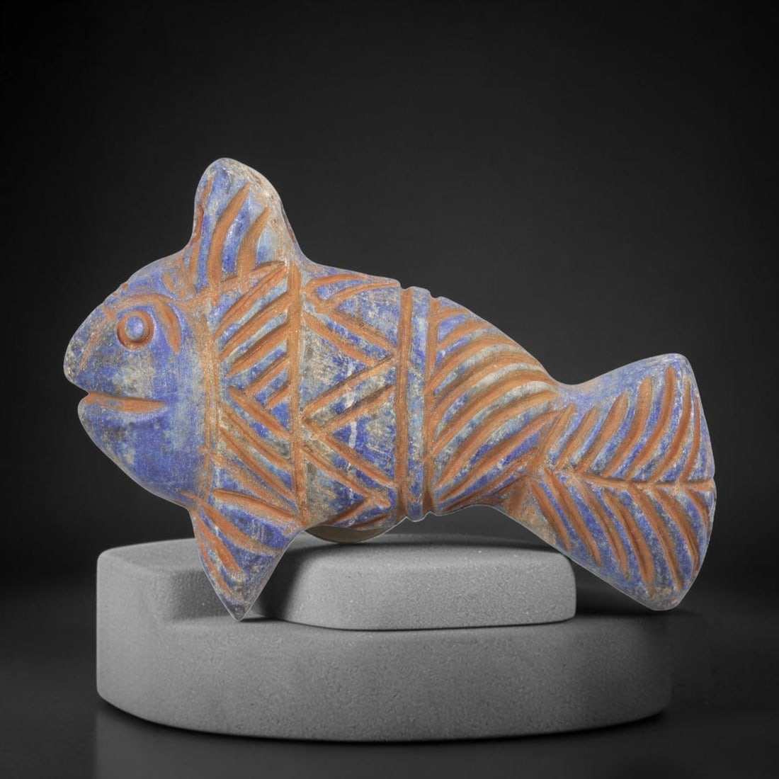 Ancient Lapis Lazuli Fish Amulet - Near Eastern Carving, 56FY: Carved from lapis lazuli, the amulet is shaped as a stylized fish, with a suspension hole drilled through the dorsal fin for wear as a protective talisman. The figure is detailed with incised geometri