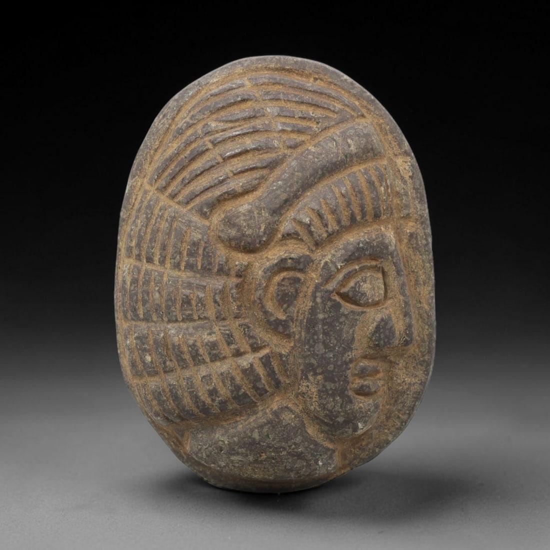 Ancient Stone Amulet - Near Eastern Bust Plaque Pendant, 18ZX: Carved from dark stone, the amulet is an oval plaque crafted in the ancient Near Eastern style, featuring a raised relief portrait of a human bust in profile. The surface bears incised details renderi