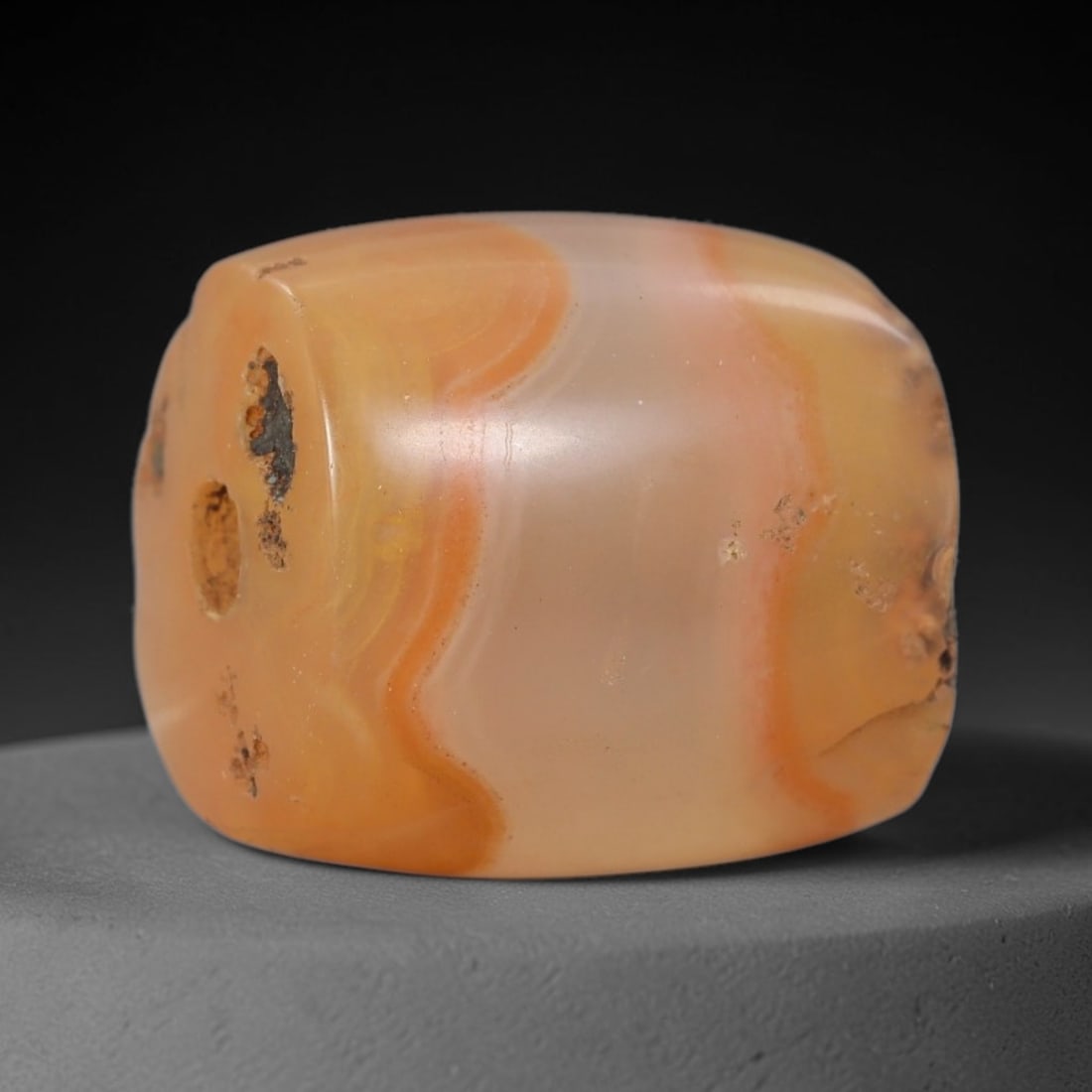 Ancient Agate Bead - Near Eastern Artifact, 4BD: This artifact is crafted from translucent banded agate, shaped into a short, cylindrical barrel form with striking warm orange and cream natural banding. The bead features a central perforation for su