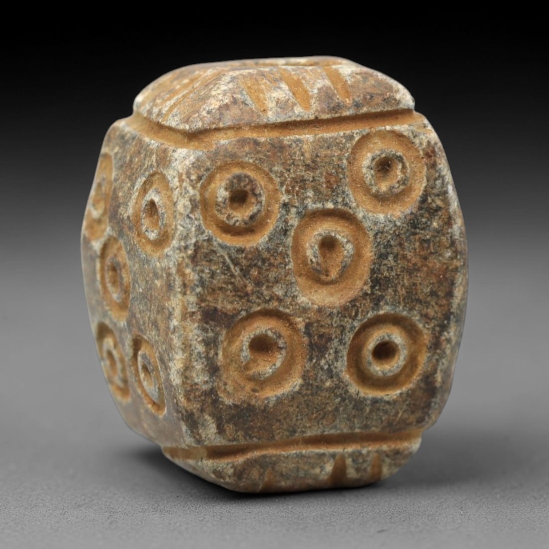 Ancient Steatite Amulet Bead - Near Eastern Concentric Circles, 47XV: Carved from granular steatite, this ancient amulet bead features a faceted, cube-like form with a vertical suspension hole at the top, designed for wearable use. Its multiple visible faces are decorat
