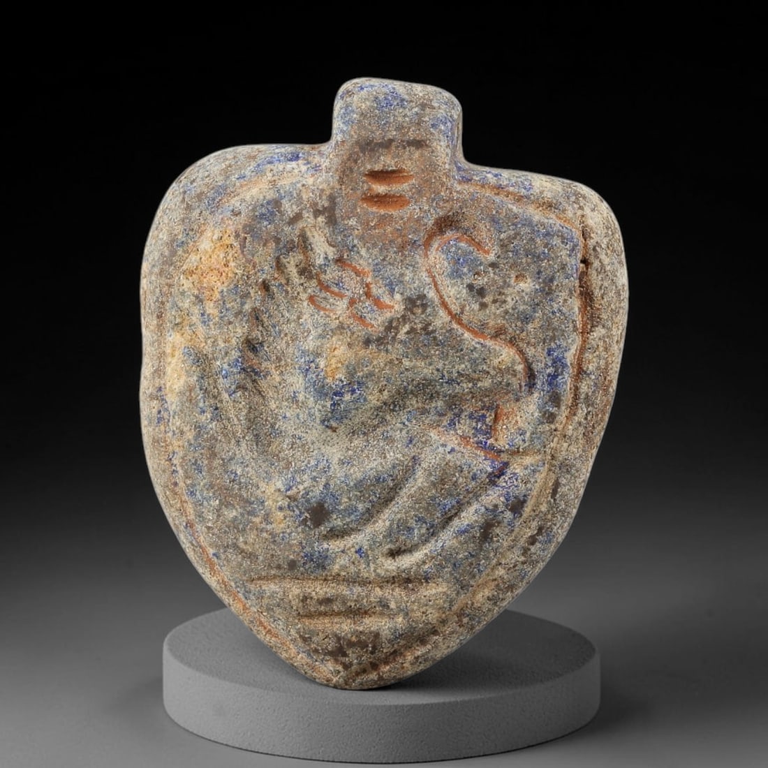 Ancient Lapis Lazuli Amulet - Near Eastern Anthropomorphic Figurine, 17BA: Carved from lapis lazuli, the amulet takes a heart-shaped form with a suspension loop at the top, designed for wear as a protective talisman. The front face is incised with a stylized anthropomorphic