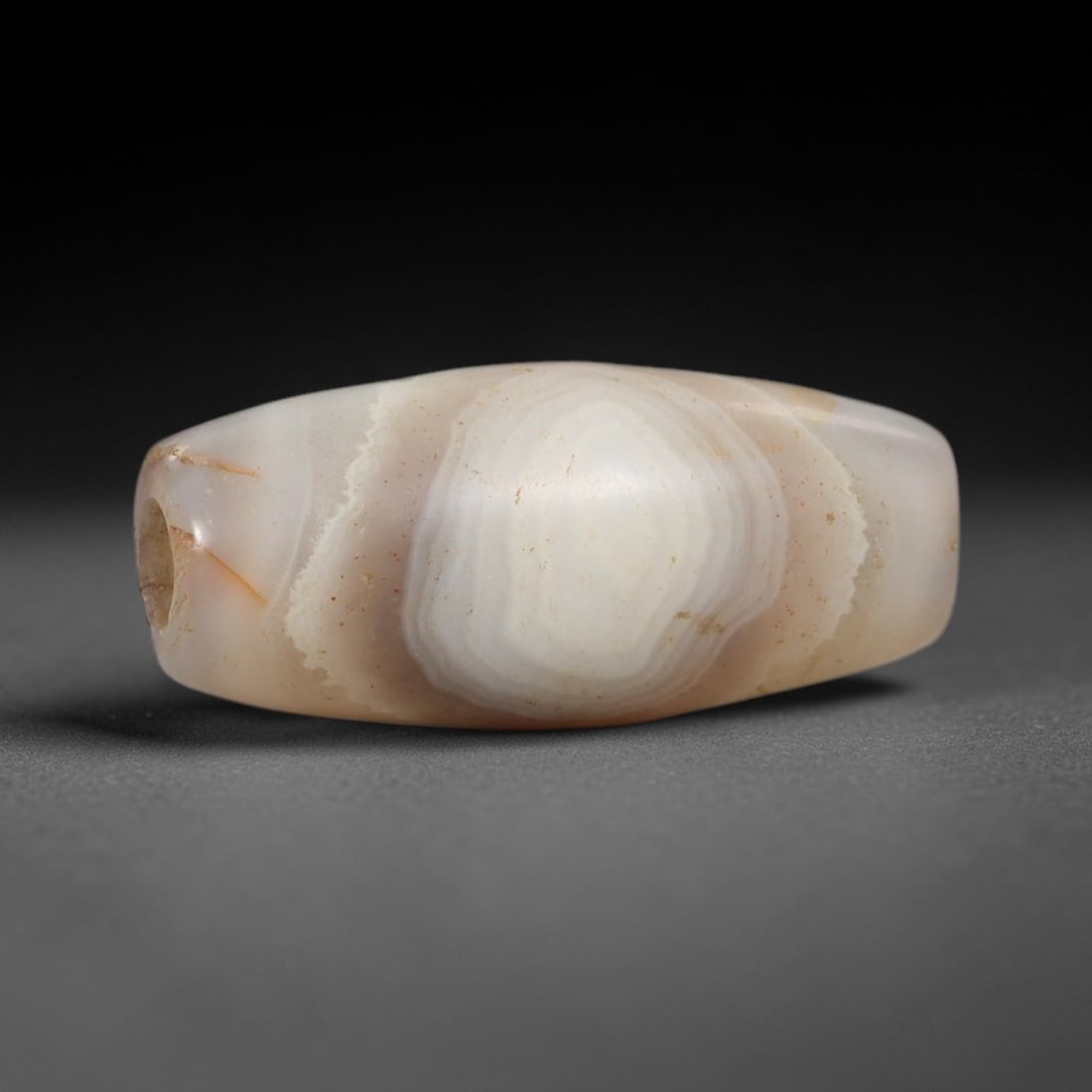 Ancient Banded Agate Bead - Silk Road Indus Valley Bicone Bead, 19BC: Carved from banded agate, the bead is fashioned in a slender bicone form, with a central drilled perforation for suspension. The stone exhibits a striking concentric "eye" banding pattern in milky whi