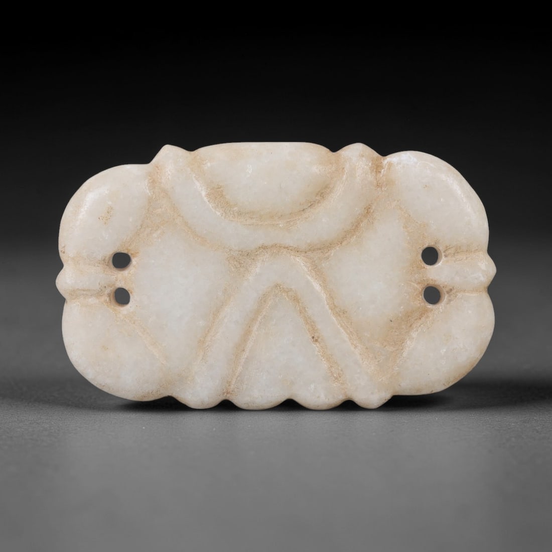 Ancient Marble Amulet - Near Eastern Ritual Pendant, 24AK: Crafted from pale marble, this amulet features a symmetrical, lobed form with scalloped lower edges. The surface is adorned with incised geometric motifs: a curved upper border and a central triangula