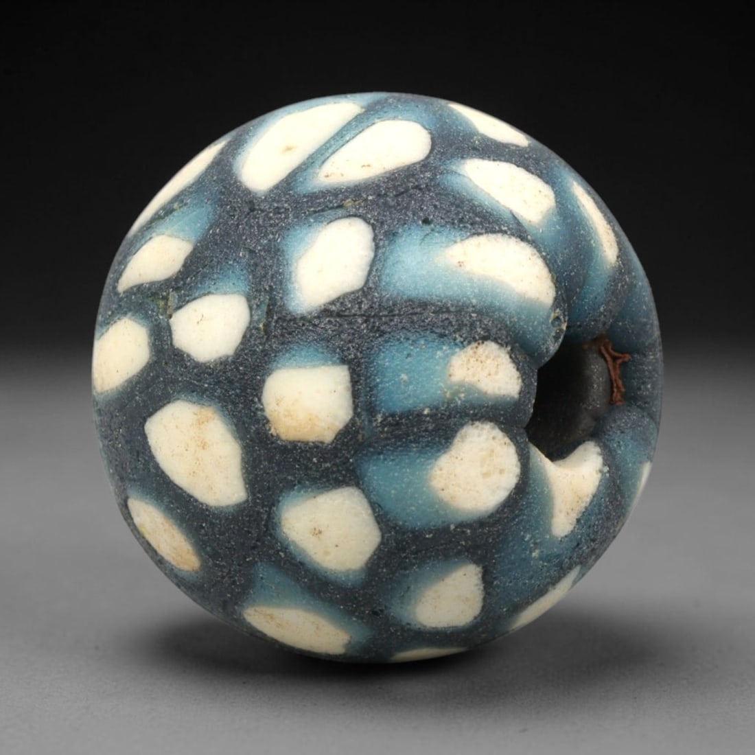 Ancient Mosaic Glass Bead - Roman Spot Pattern Amulet, 60WD: This spherical bead is crafted from core-formed mosaic glass, featuring a deep charcoal blue base decorated with irregular cream-colored glass inlays set within pale turquoise matrix, executed using t