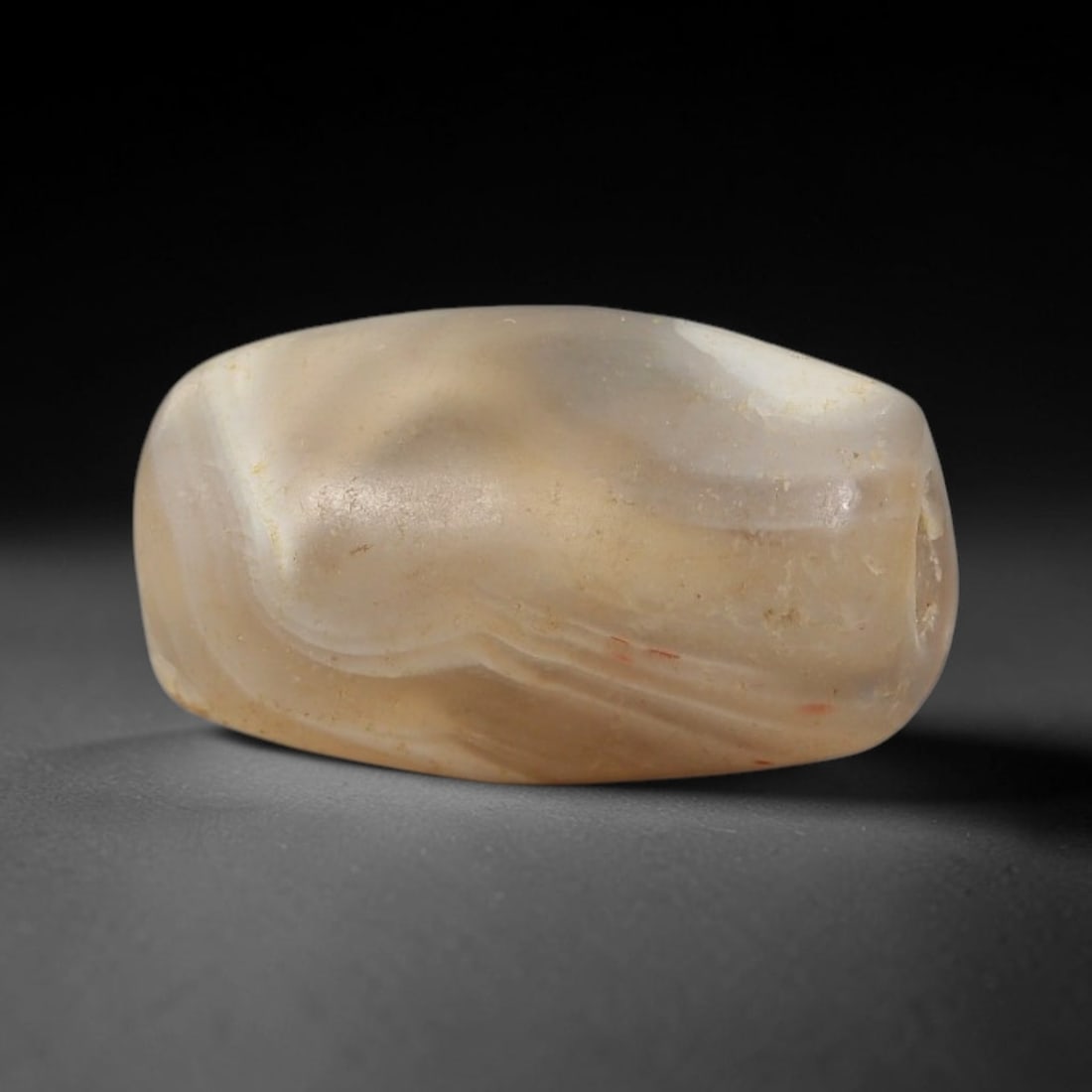 Ancient Agate Bead - Indus Valley Artifact, 45BD: This artifact is crafted from translucent agate, shaped into a compact, irregular barrel form with natural undulating contours and subtle banding. The bead features a central perforation for suspensio