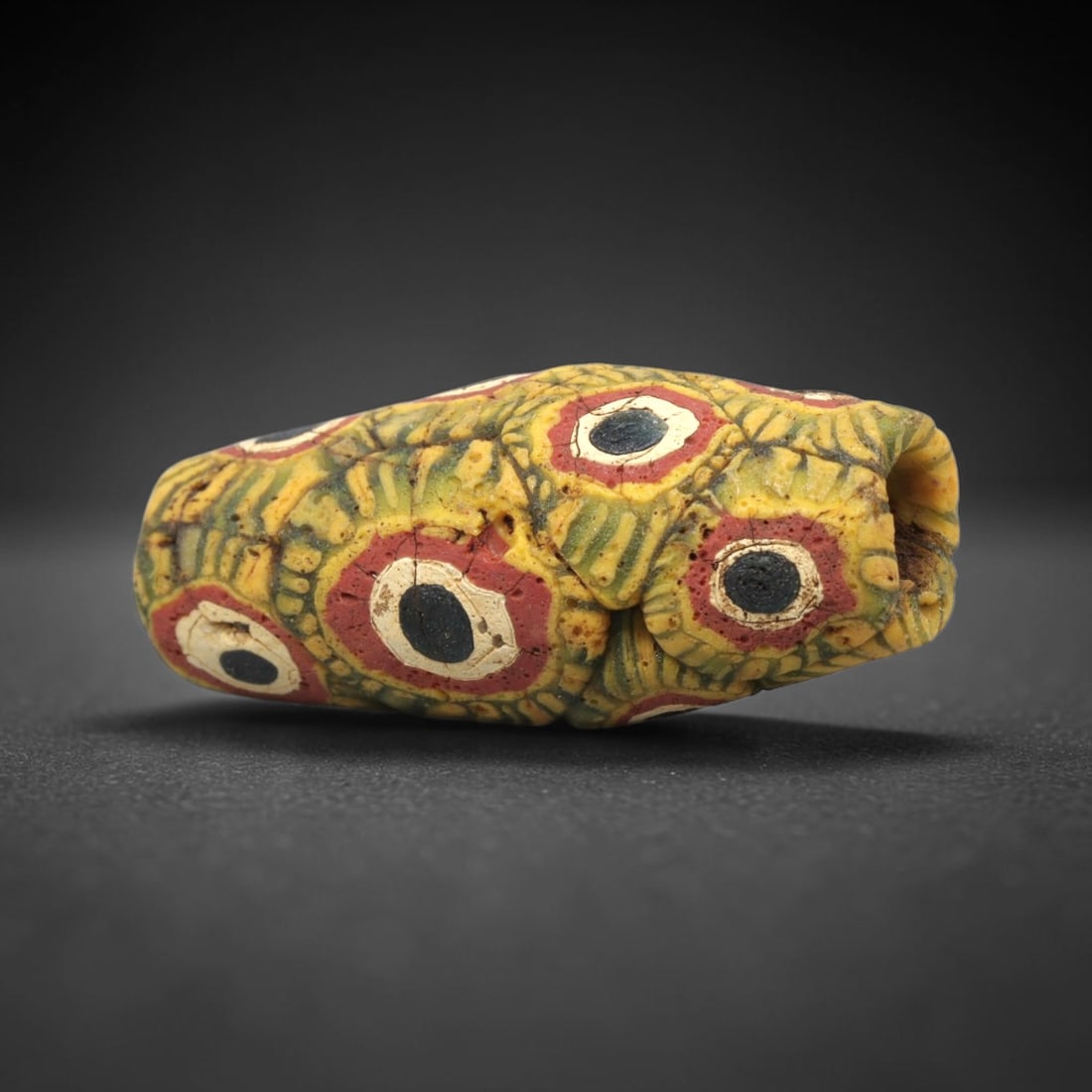 Ancient Mosaic Glass Bead - Roman Eye Pattern Amulet, 75WD: This elongated cylindrical bead is crafted from core-formed mosaic glass, featuring a vibrant yellow-green base densely decorated with multiple concentric eye motifs. Each eye motif consists of a cent