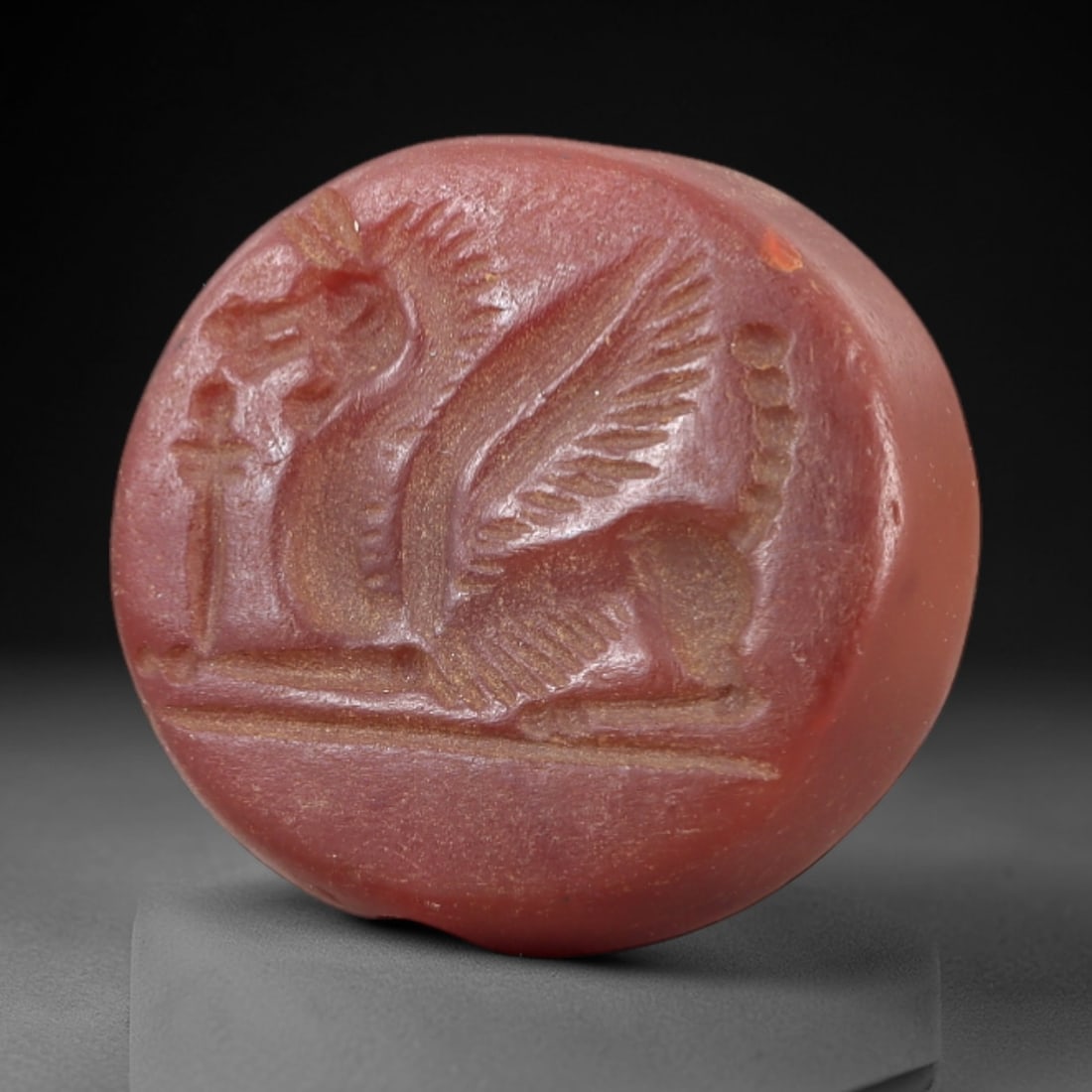 Ancient Carnelian Intaglio - Near Eastern Griffin Seal Amulet, 22AL: Crafted from deep red carnelian, this circular intaglio bears a finely incised depiction of a recumbent griffin-a mythical composite beast with avian head, feathered wings, and leonine body-accompanie