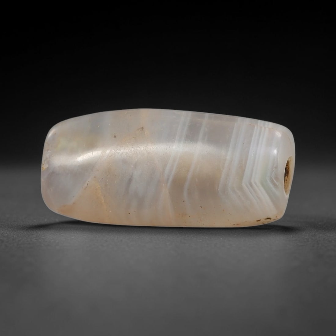 Ancient Banded Agate Bead - Indus Valley Artifact, 6BD: This artifact is crafted from translucent banded agate, shaped into a compact barrel form with distinctive chevron-style parallel banding in soft white and grey hues. The bead features a central perfo