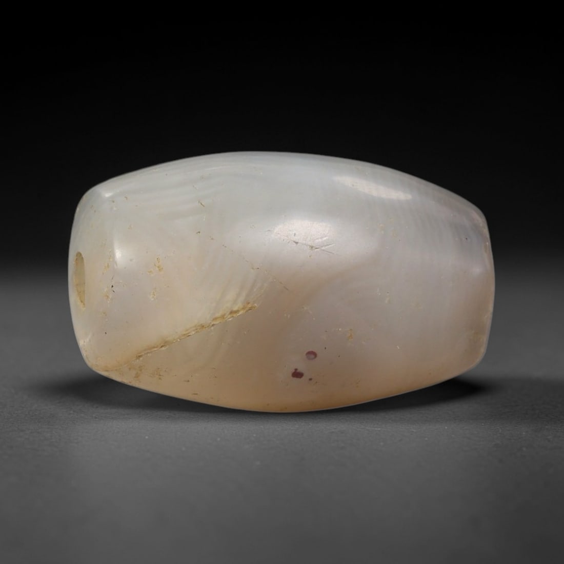 Ancient Agate Bead - Silk Road Amulet, 32BC: This artifact is crafted from pale creamy white agate, exhibiting fine, subtle wavy banding across its smooth rounded barrel form, shaped through precise ancient lapidary craftsmanship. The bead featu