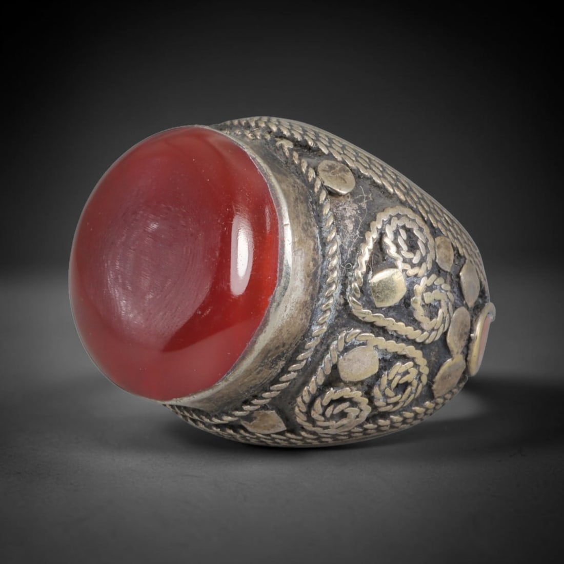 Antique Silvered Ring - Eurasian Steppe Carnelian Cabochon, 17BK: Silvered metal ring featuring a large, smooth domed carnelian cabochon at the center, framed by twisted ropework. The band displays intricate pseudo-filigree coiled and braided motifs, raised dot and 