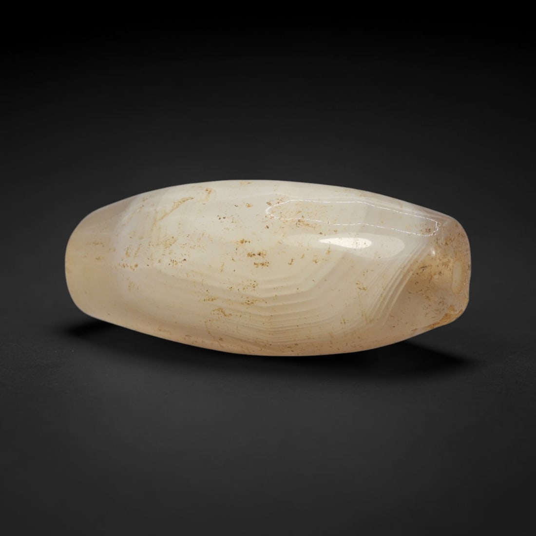 Ancient Agate Bead - Indus Valley Banded Carving, 63WJ: This artifact is crafted from banded agate, featuring elegant, subtle banding in creamy off-white and pale amber hues across its smooth, polished surface. The bead is shaped in a streamlined, tapered 