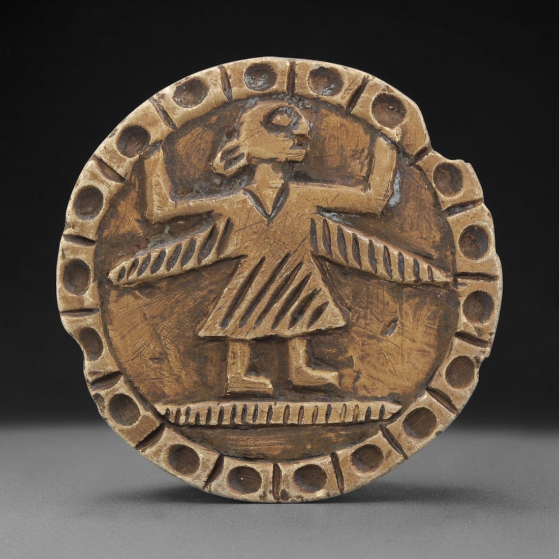 Ancient Steatite Plaque - Near Eastern Winged Figure Relief, 29ZY: Carved from steatite, this circular plaque features a relief depiction of a winged anthropomorphic figure, rendered in the stylized, schematic artistic tradition of the Ancient Near East. The figure s